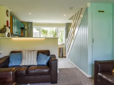 a living room with a leather couch and a staircase at Fifty Six in Saint Columb Major