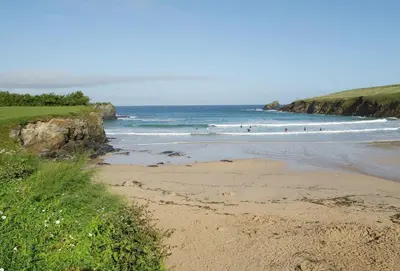 a beach with people surfing in the ocean at Brook Cottage Cornwall in St Merryn