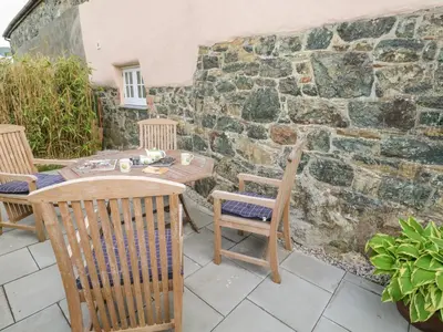 a patio with a table and chairs and a stone wall at Gilly Skyber in Helston