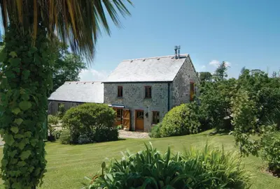 an old stone house on a lawn with a palm tree at Tregadjack Barn in Crowan