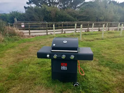 a grill sitting in the grass next to a fence at Hawk's View Bell Tent at Higher Hawksland Farm in Saint Issey