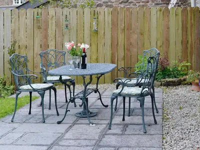a patio table and chairs with a vase of flowers at Barton Cottage in North Petherwin
