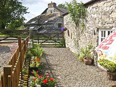 a stone house with a wooden fence and flowers at Dove Cottage in Lezant