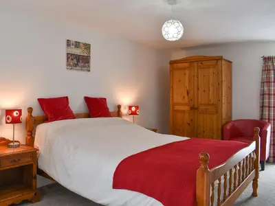 a bedroom with a large bed and a red chair at Dove Cottage in Lezant