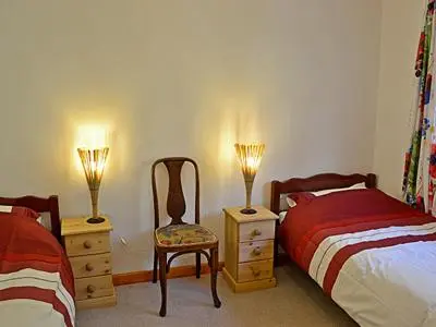 a bedroom with two beds and a chair and two lamps at Ponsgwedhen in Coverack
