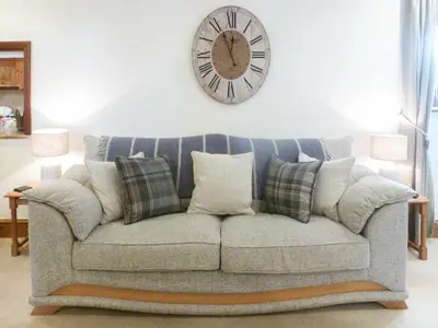 a couch with pillows and a clock on the wall at Anneth Lowen in Pentewan