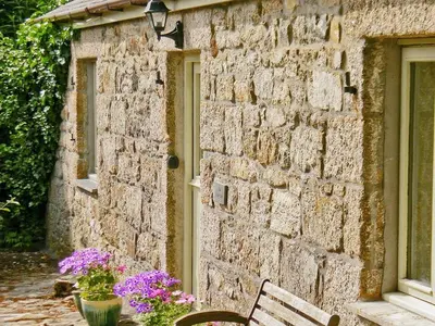 a stone building with a bench and flowers in front of it at The Long Barn in Crowan