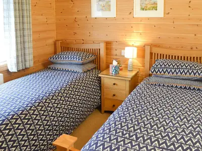 a bedroom with two beds and a wooden wall at Wheal Metal Lodge in Carleen