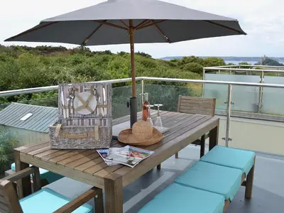 a wooden table with an umbrella on a balcony at Beach Comber Cottage in Marazion