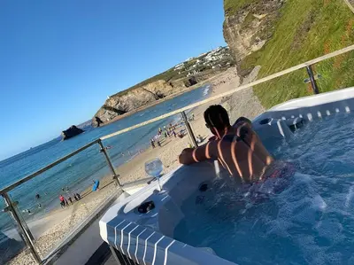 a person in a hot tub next to a beach at Award Winning 5* BEACH HOUSE! Hot Tub & Fire Pit in Portreath