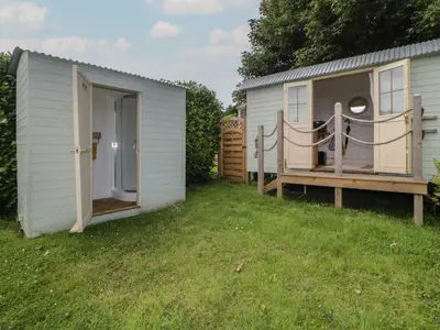 a small white shed with a porch and a yard at Flora's Hut in Liskeard