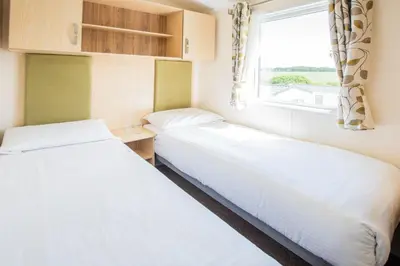 two beds in a small room with a window at Killigarth Manor Holiday Park in Polperro