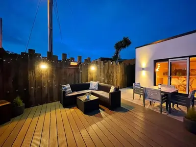 a deck with a couch and chairs and a table at Littlecroft, Hollywell Bay by Together Travel - Luxury Seaside Cottage Retreat in Holywell Bay