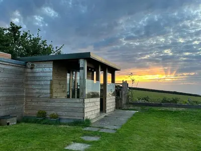 a small cabin in a field with the sunset in the background at Little Swelle Cabin with awesome Sea views in Poundstock