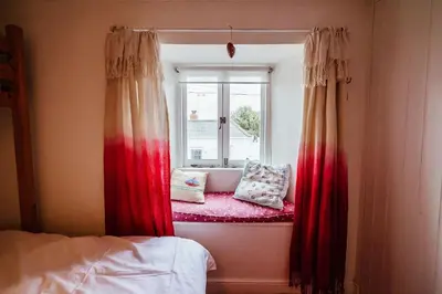 a window seat in a bedroom with red curtains at Roses Cottage in Porthscatho