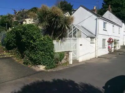 a white house with a palm tree next to a street at Roses Cottage in Porthscatho