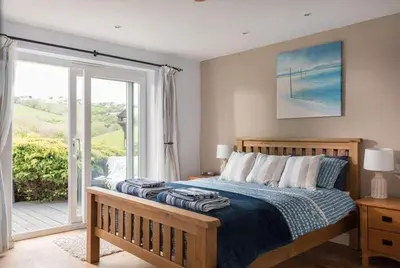 a bedroom with a bed and a sliding glass door at Cosy Beachfront Retreat with Stunning Sea Views & Free Access to a Local Indoor Pool in Talland