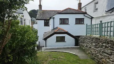 a white house with a fence and a stone wall at Hillside Cottage in Porthscatho