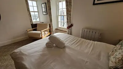a bedroom with a bed and a chair and windows at Hillside Cottage in Porthscatho