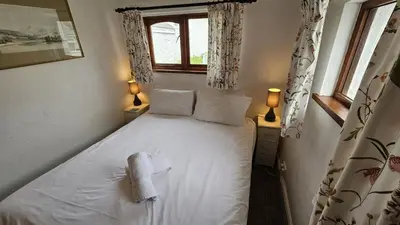 a small bedroom with a white bed with a window at Hillside Cottage in Porthscatho