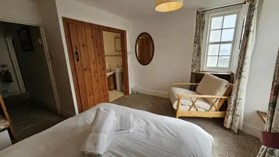 a bedroom with a bed and a chair and a window at Hillside Cottage in Porthscatho