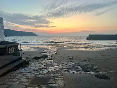 a stone walkway leading to the ocean at sunset at Ebb Tide - Fisherman's Cottage in Gorran Haven