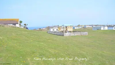 a grassy hill with houses and the ocean in the background at A17 Placerville, Riviere Towans in Hayle