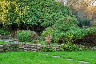 a garden with a stone wall in the grass at Finest Retreats - The Old Counting House in Gweek