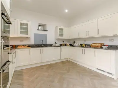a white kitchen with white cabinets and a wooden floor at 4 Bed in Callington oc-54343 in Linkinhorne