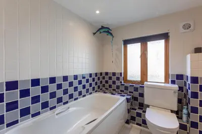 a bathroom with a tub and a toilet and blue tiles at Sunset View in Bude