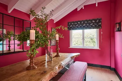 a pink room with a wooden table and a window at Lostwithiel Dairy House in Braddock