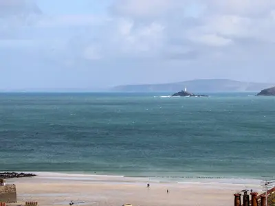 a beach with a lighthouse in the ocean at Rooftops in St Ives