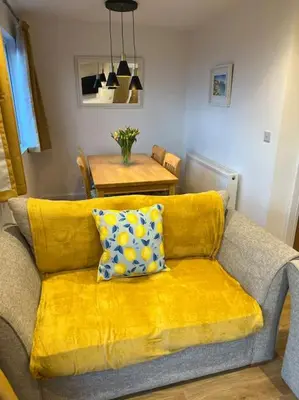 a yellow couch with a pillow on it in a living room at Citrus Chalet, modern light and airy! in Redruth