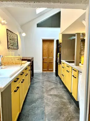 a large kitchen with yellow cabinets and a sink at Little Hillside in Porthtowan
