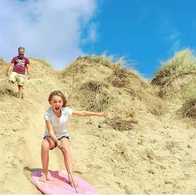 a little girl sitting on a surfboard on the beach at Heart of Kernow Holidays in Bugle