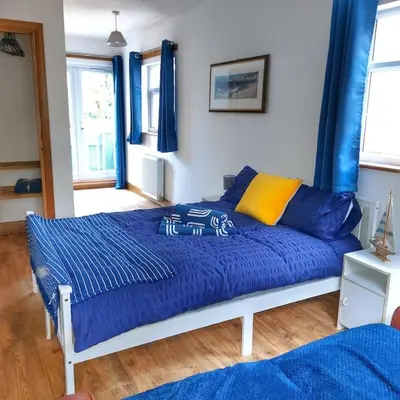 a bedroom with a bed with blue sheets and windows at Heart of Kernow Holidays in Bugle