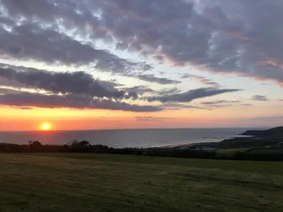 a sunset over the ocean with a grass field at Bungalow 19 in Poundstock