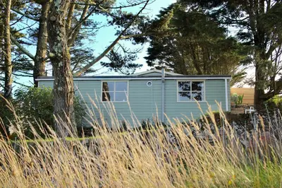 a small blue house in a field of tall grass at Scandi Cabin On A Hill, With Stunning Views Across Cornwall in Nancledra