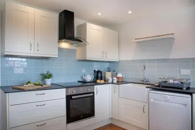 a kitchen with white cabinets and blue tiles at Meadow House in Porthscatho