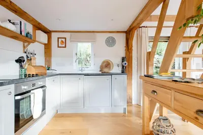 a kitchen with white cabinets and a wooden floor at Little Trenant Barn on Helford River Near Constantine in Constantine