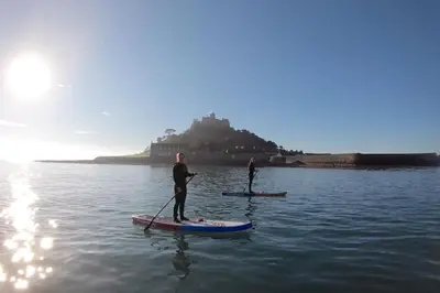 two people are standing on paddle boards in the water at Rymer-Leigh in Marazion