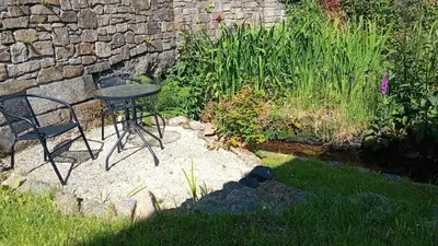 a table and chairs in a garden with a stone wall at River Cottage, Chypons Farm, Rural St Ives in Nancledra