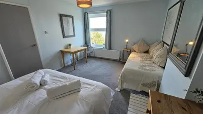 a bedroom with two beds and a table and a window at Chywartha in Porthscatho