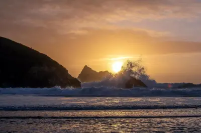 a sunset over the ocean with a wave crashing on the rocks at 3 Waves in Newquay