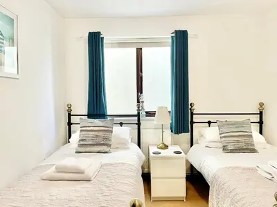 two beds in a room with blue curtains at April Cottage in Padstow