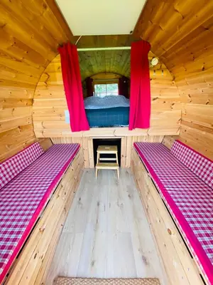 a room with two beds in a wooden cabin with red curtains at Barrel Cabin 1 in St Austell