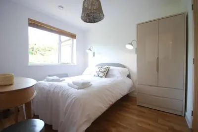 a white bedroom with a bed and a window at Anemone in Porthtowan