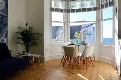 a dining room with a table and chairs and windows at Flip Flop Flat, Sea Views, Short Stroll to Beaches in Newquay