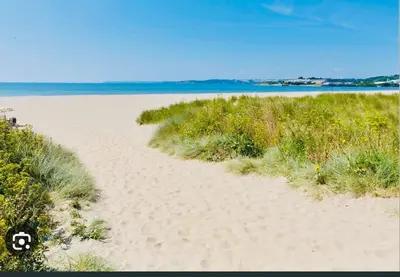 a sandy beach with grass and the ocean in the background at The Lobster Pot in Tywardreath