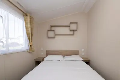 a bedroom with a large white bed with a window at Tencreek Holiday Park in Looe